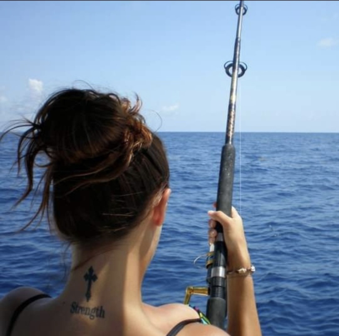Nikki from behind, holding a fishing rod over deep blue open water.