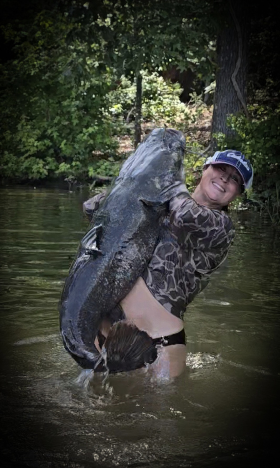 Nikki in a camo shirt heaving a giant catfish up out of the water.