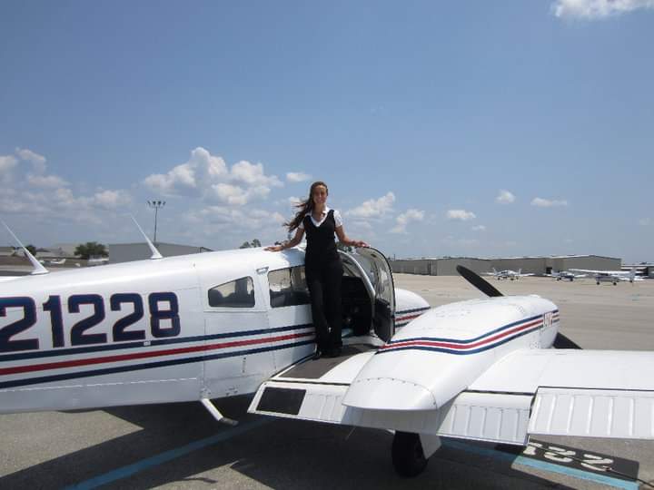 Nikki standing in the doorway on the wing of Piper N21228, hair blowing.