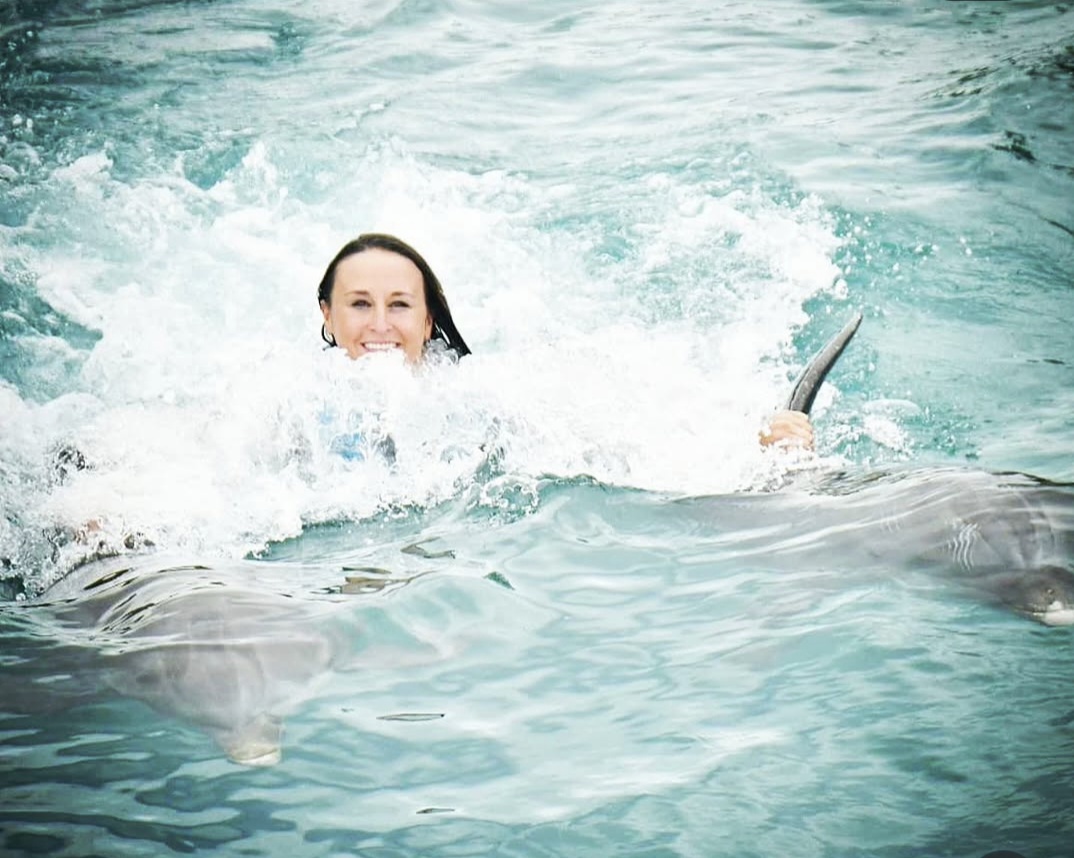 Nikki grinning through the spray as the dolphins pull her along.