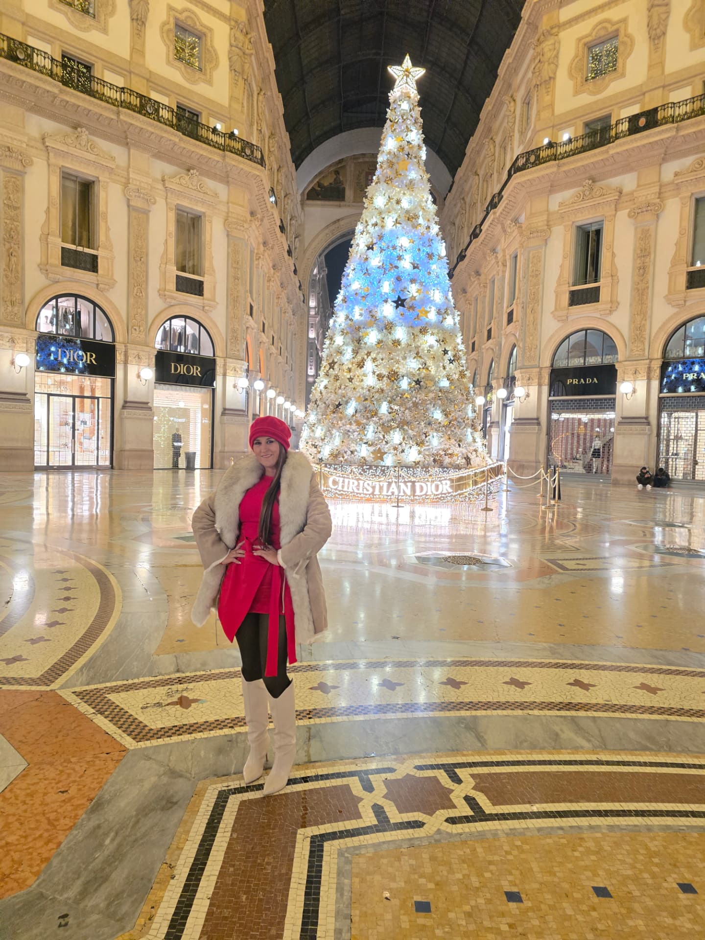 Nikki Bodie standing alone on the mosaic floor of the nearly empty Galleria Vittorio Emanuele II at night, the Christmas tree behind her.