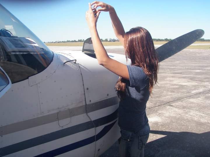 Nikki checking the top of a Cessna's cowling on a sunny ramp.