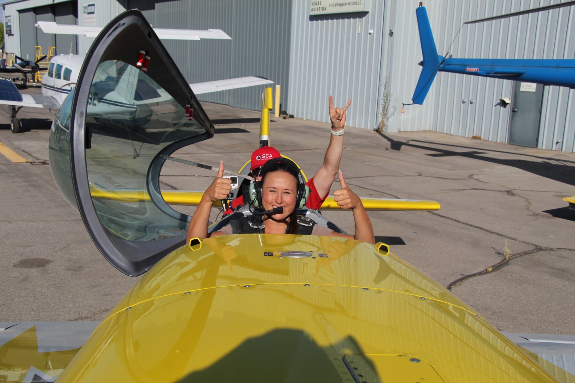 Nikki cheering in the cockpit of a yellow aerobatic airplane.