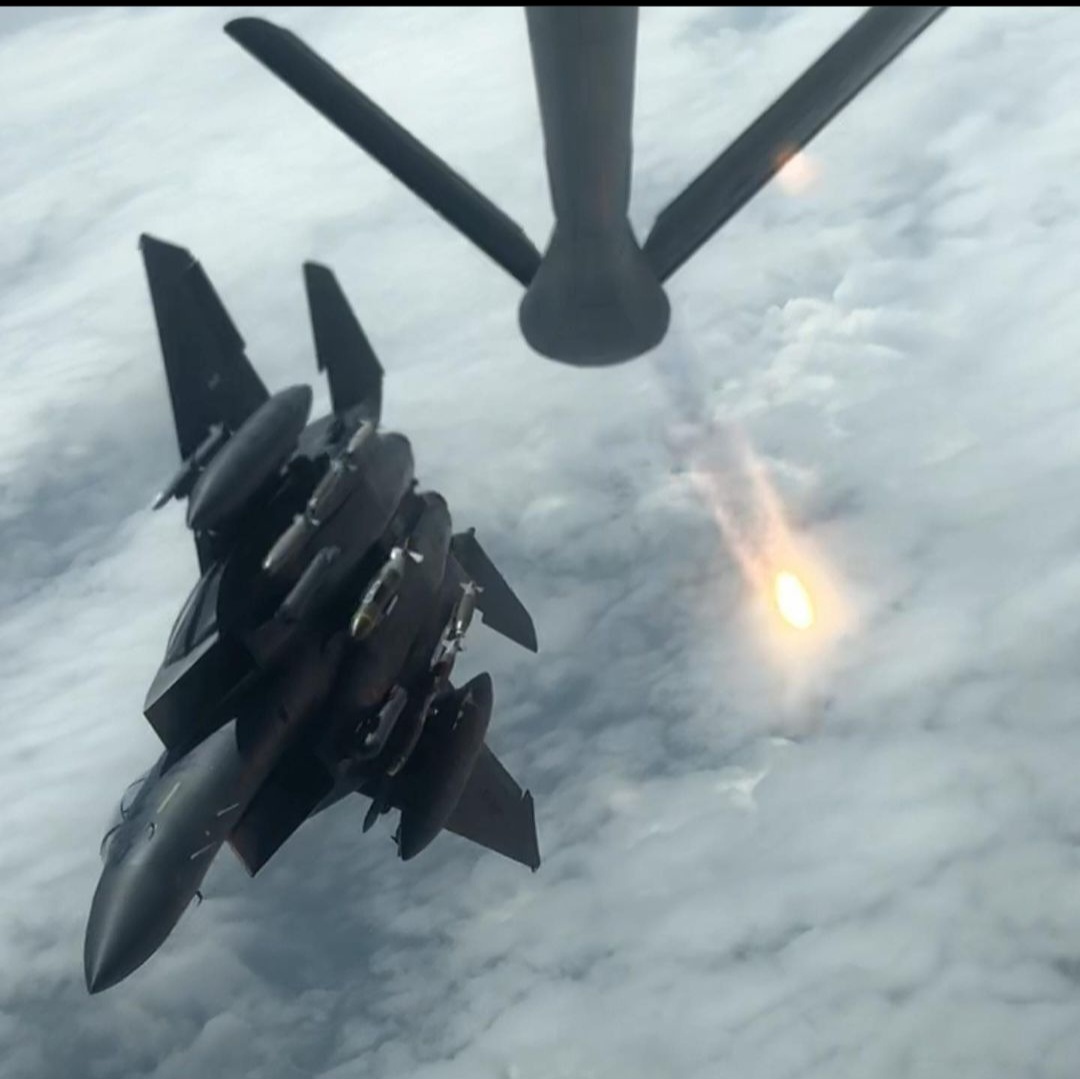 A fighter under the refueling boom as a flare burns off.