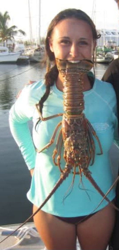 Nikki on a dock holding a spiny lobster in her teeth.
