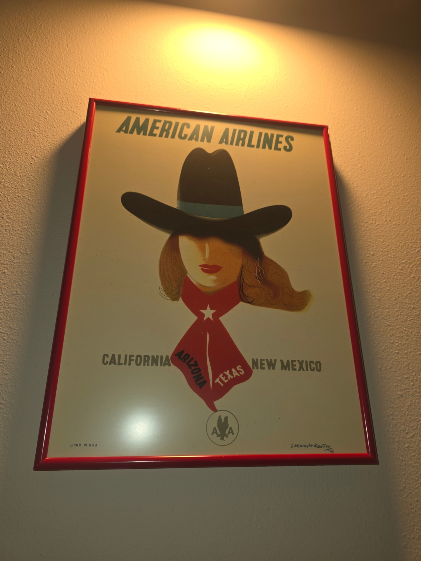 A vintage American Airlines poster of a woman in a cowboy hat, framed on the Airbnb wall.