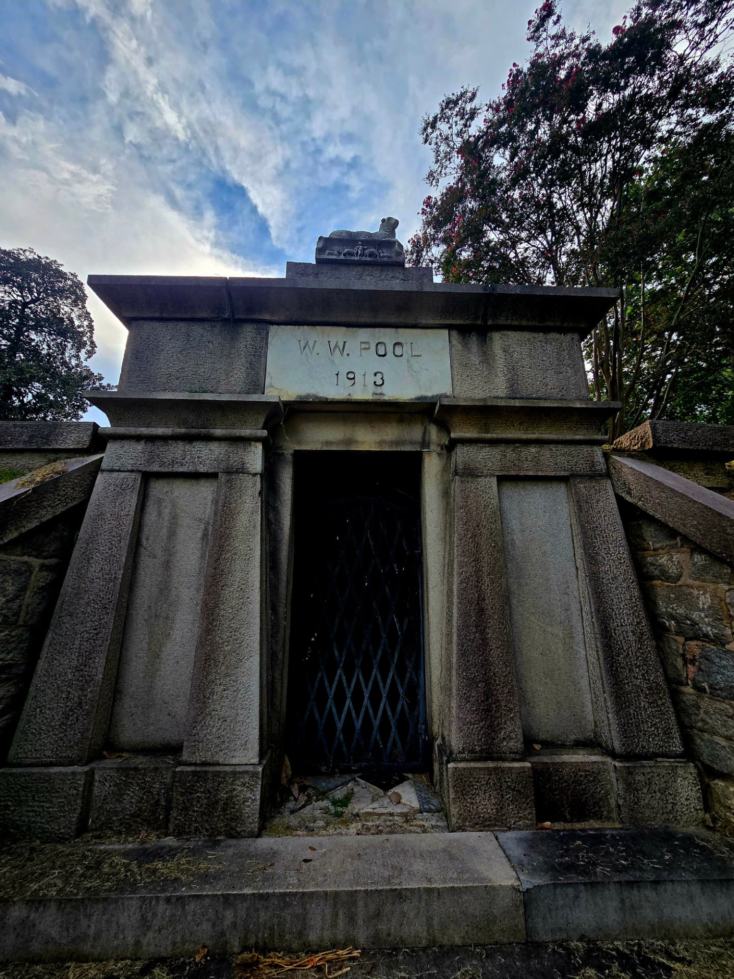 The W. W. Pool mausoleum in Hollywood Cemetery, dated 1913, with a stone dog atop its roof against a clouded sky.