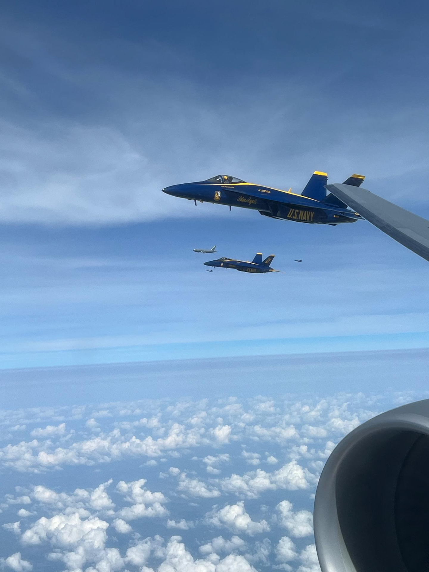 Blue Angels flying off the tanker's wing above a field of clouds.