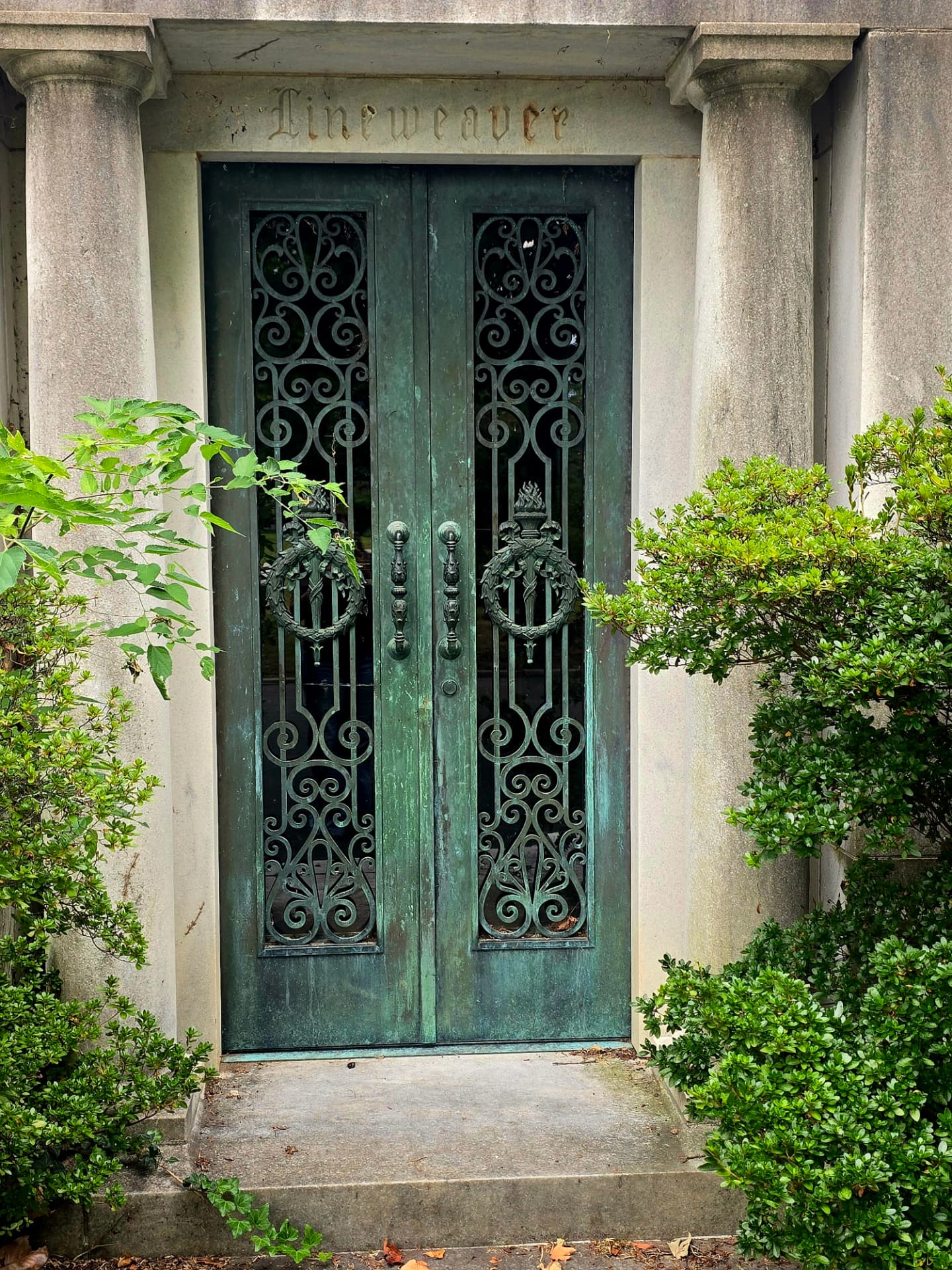 A pair of verdigris bronze mausoleum doors with ornate scrollwork grilles, the name Lineweaver carved in the stone lintel above them.