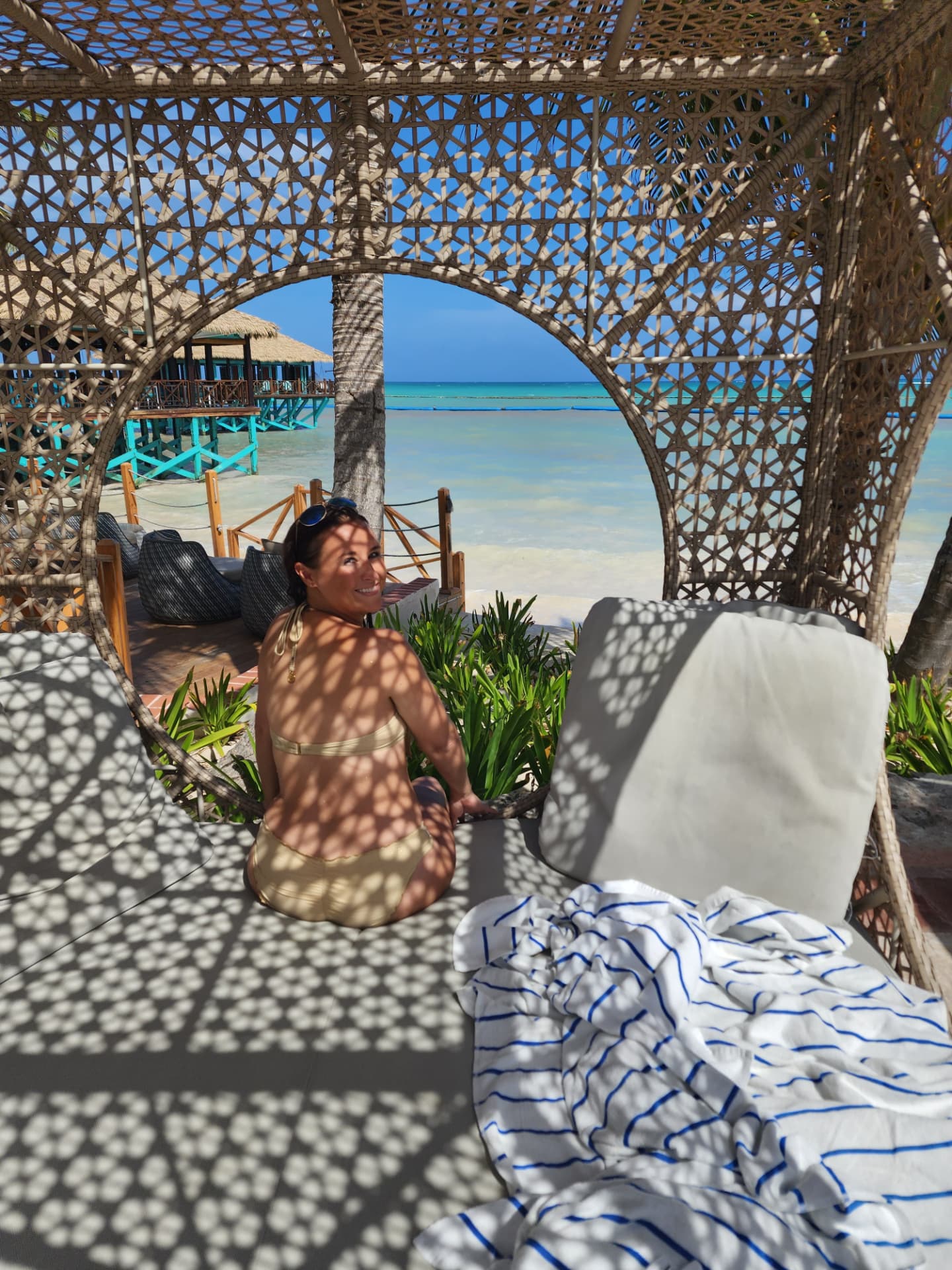 Nikki Bodie looking back from a woven beach cabana onto turquoise water and thatched huts.
