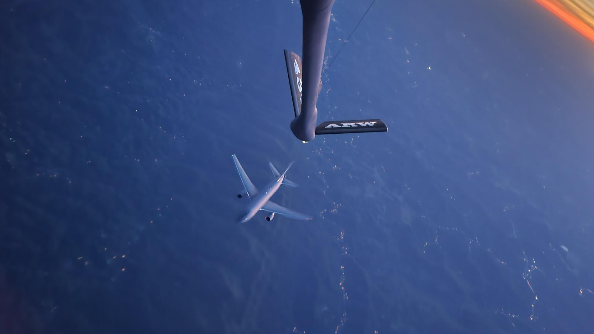 The refueling boom at dusk with another tanker far below over city lights.