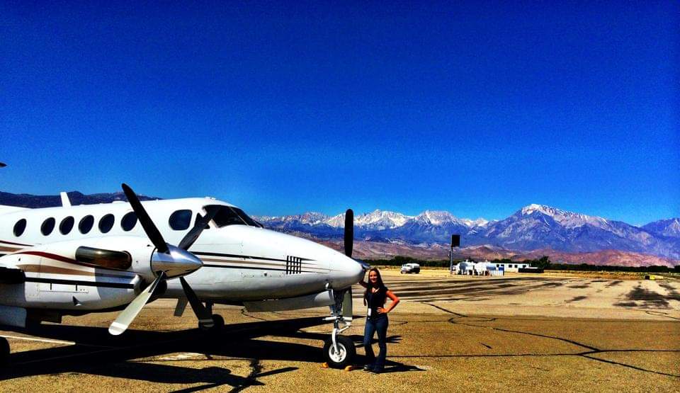 Nikki Bodie beside a King Air turboprop on the ramp beneath the snow-capped Sierra Nevada.