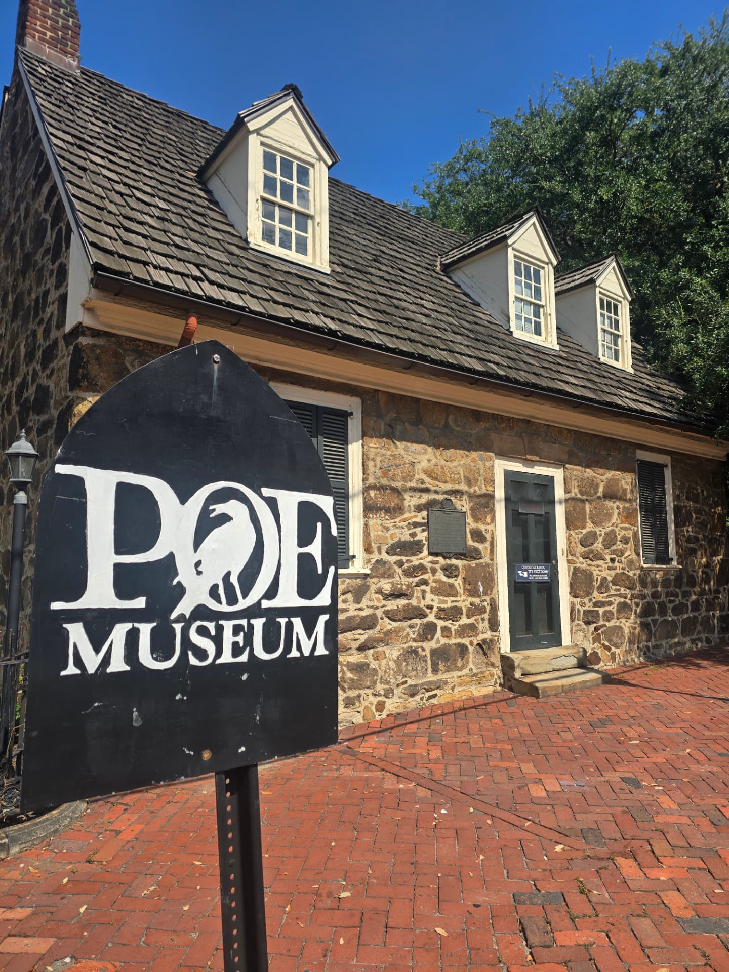 The stone Old Stone House at the Poe Museum in Richmond, its black arched sign reading POE MUSEUM in the foreground under a clear blue sky.