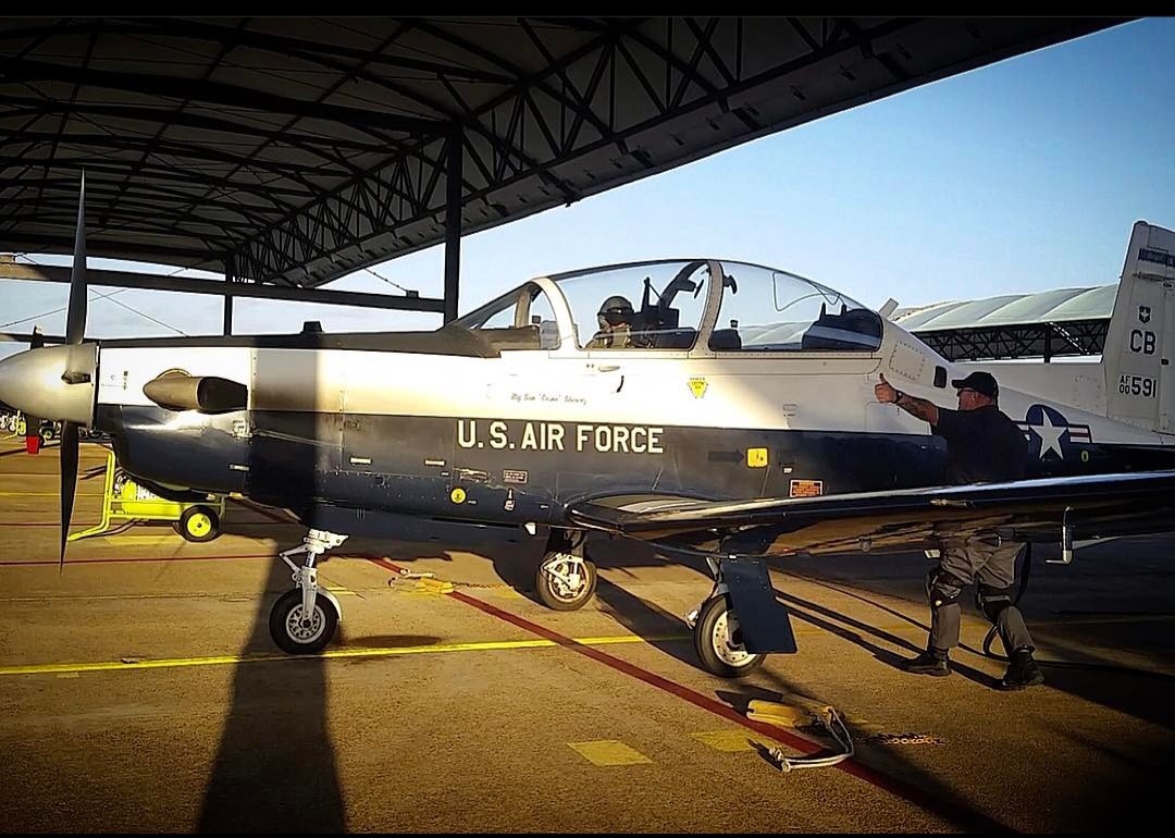 A T-6 under the sunshade, crew chief giving a thumbs-up to the pilot.
