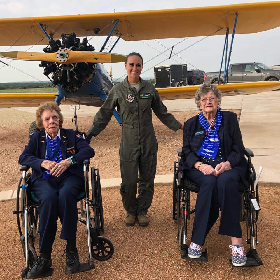 Nikki in her flight suit standing between two WASP in front of a yellow biplane.
