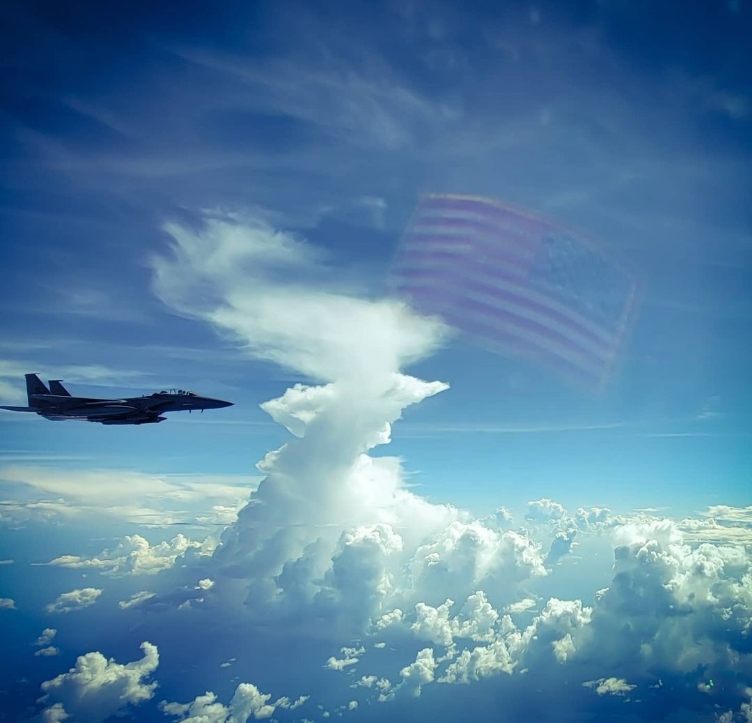 A fighter beside a towering storm cloud, the flag reflected in the window.