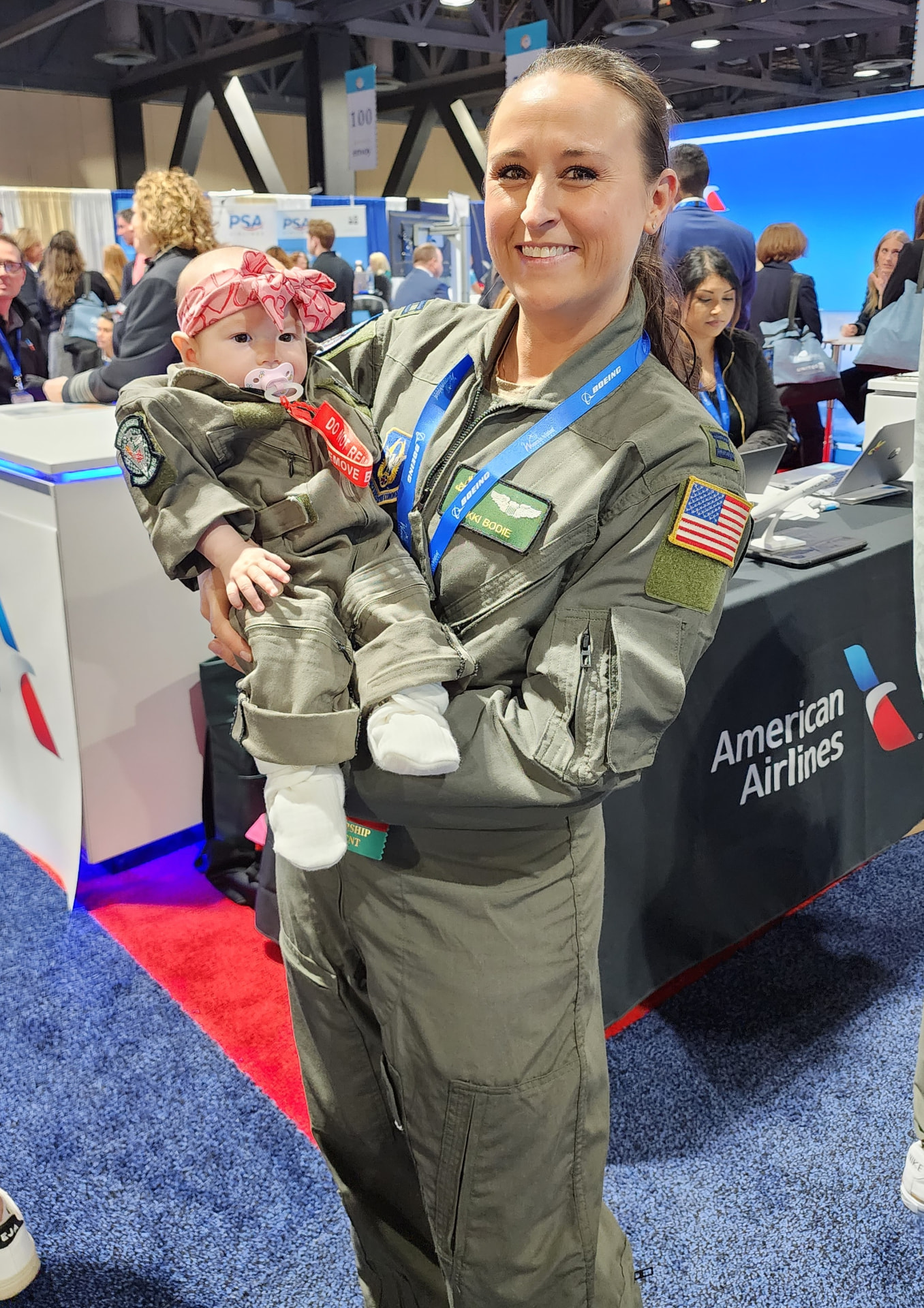 Nikki holding a friend's baby dressed in a tiny flight suit at a recruiting conference.