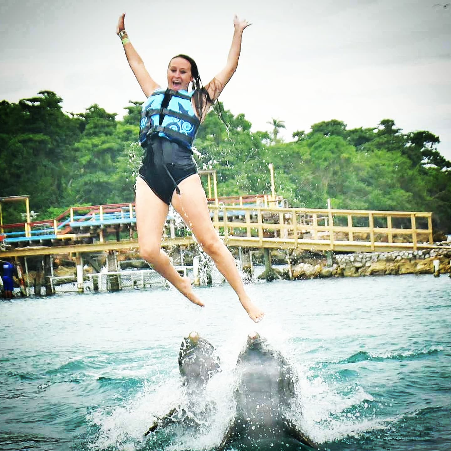 Nikki launched into the air, arms raised, her feet just leaving the noses of two dolphins.