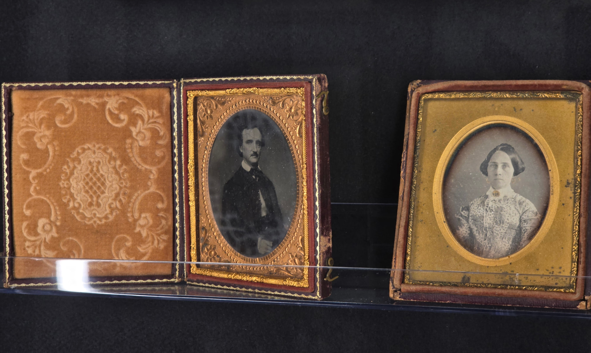 Two cased daguerreotypes side by side in a museum vitrine: a portrait of Edgar Allan Poe and a portrait of a young woman.