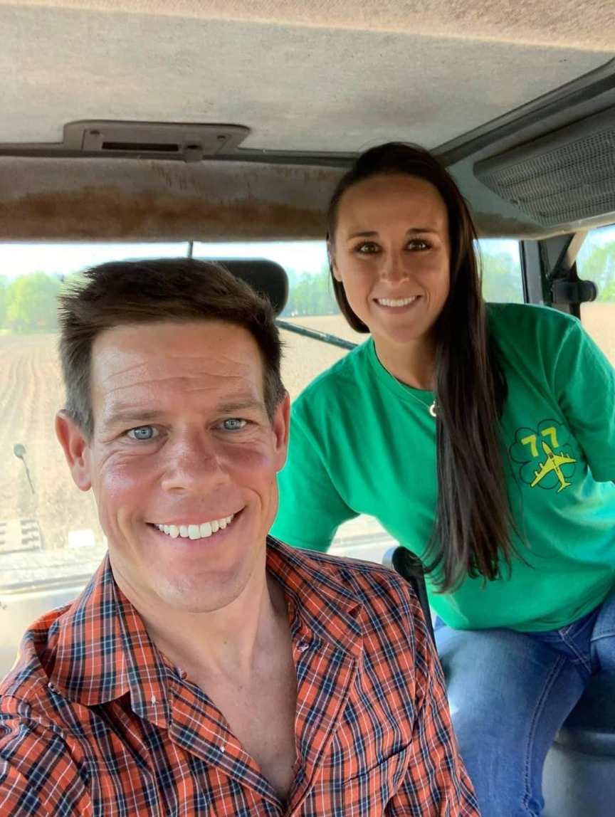 Nikki Bodie and Quentin smiling together inside a tractor cab above a freshly planted Wisconsin field.
