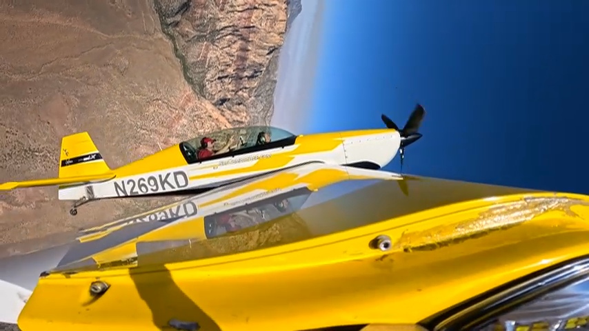 A yellow aerobatic airplane in formation over the canyon.