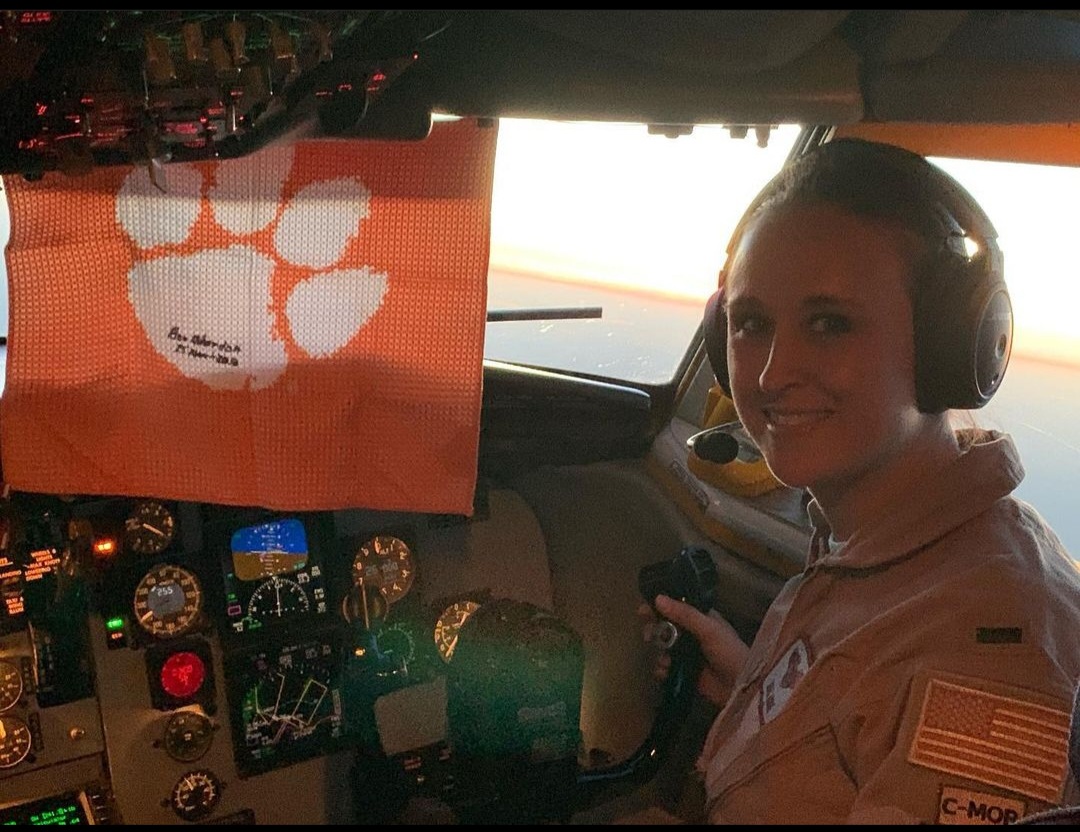 Nikki smiling in her headset with a Clemson towel hung in the cockpit.