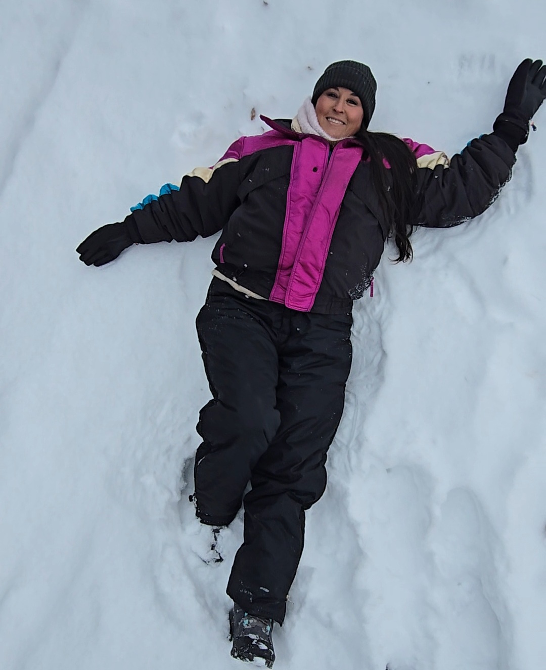 Nikki Bodie in a pink and black snowsuit making a snow angel in fresh powder.
