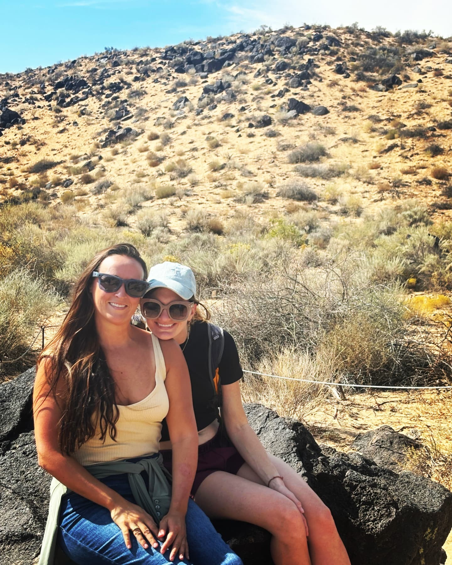 Nikki and Ali smiling together on a rock in the New Mexico desert.