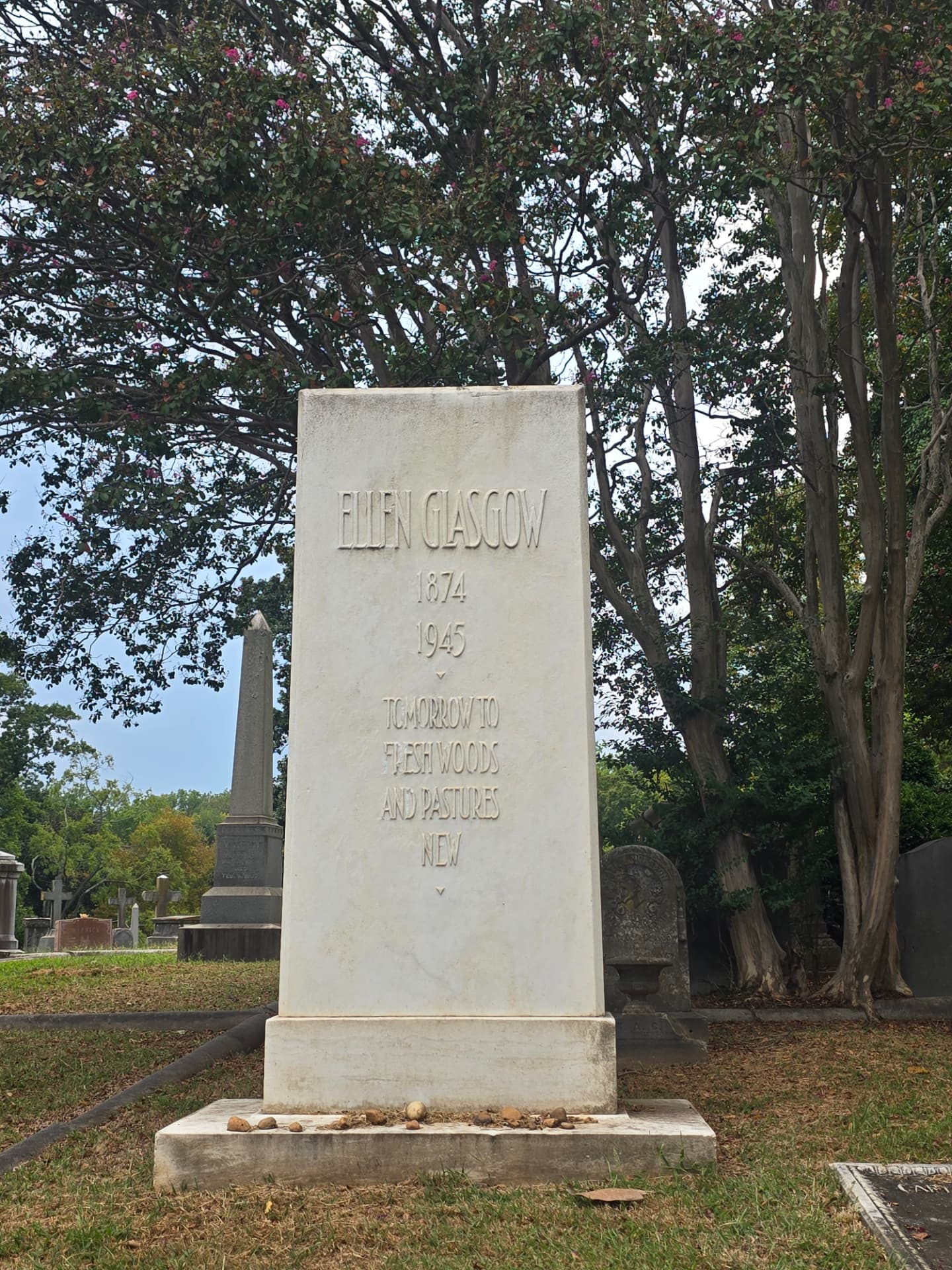 Ellen Glasgow's spare white marble monument in Hollywood Cemetery, carved with her name, 1874-1945, and the line "Tomorrow to fresh woods and pastures new," small stones left along its base.