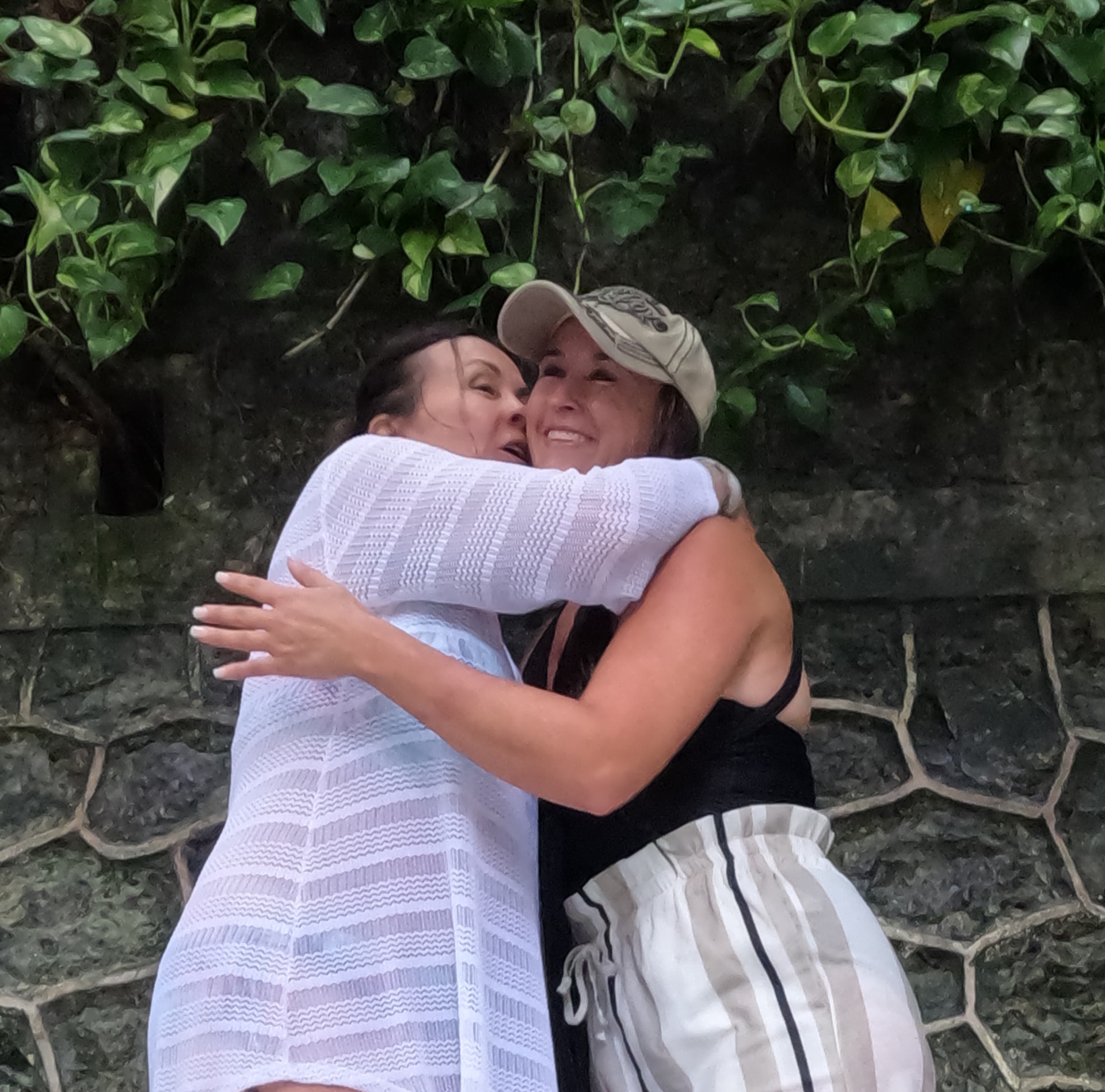Patti hugging Nikki tightly beneath hanging vines, both smiling.