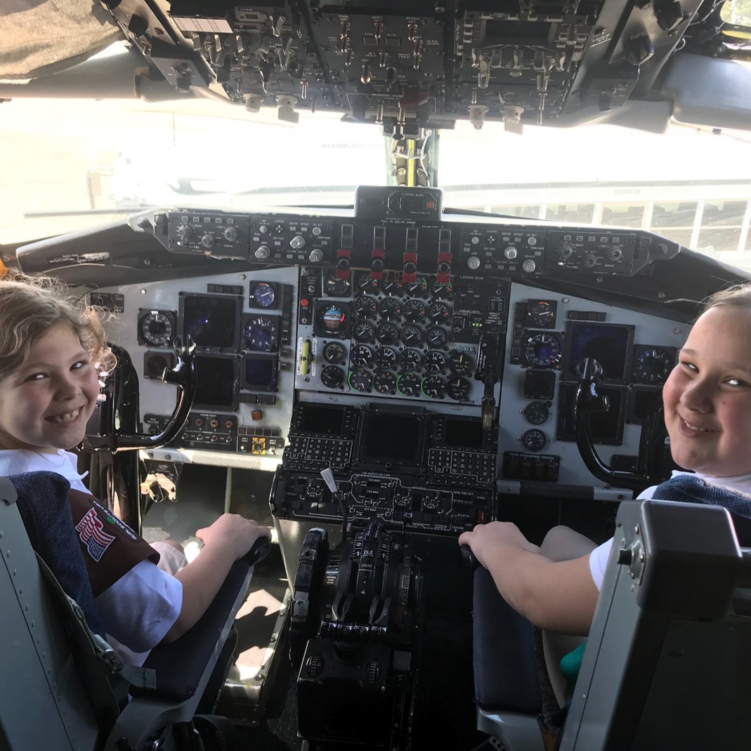 Two young Girl Scouts grinning from the pilots' seats of a KC-135.
