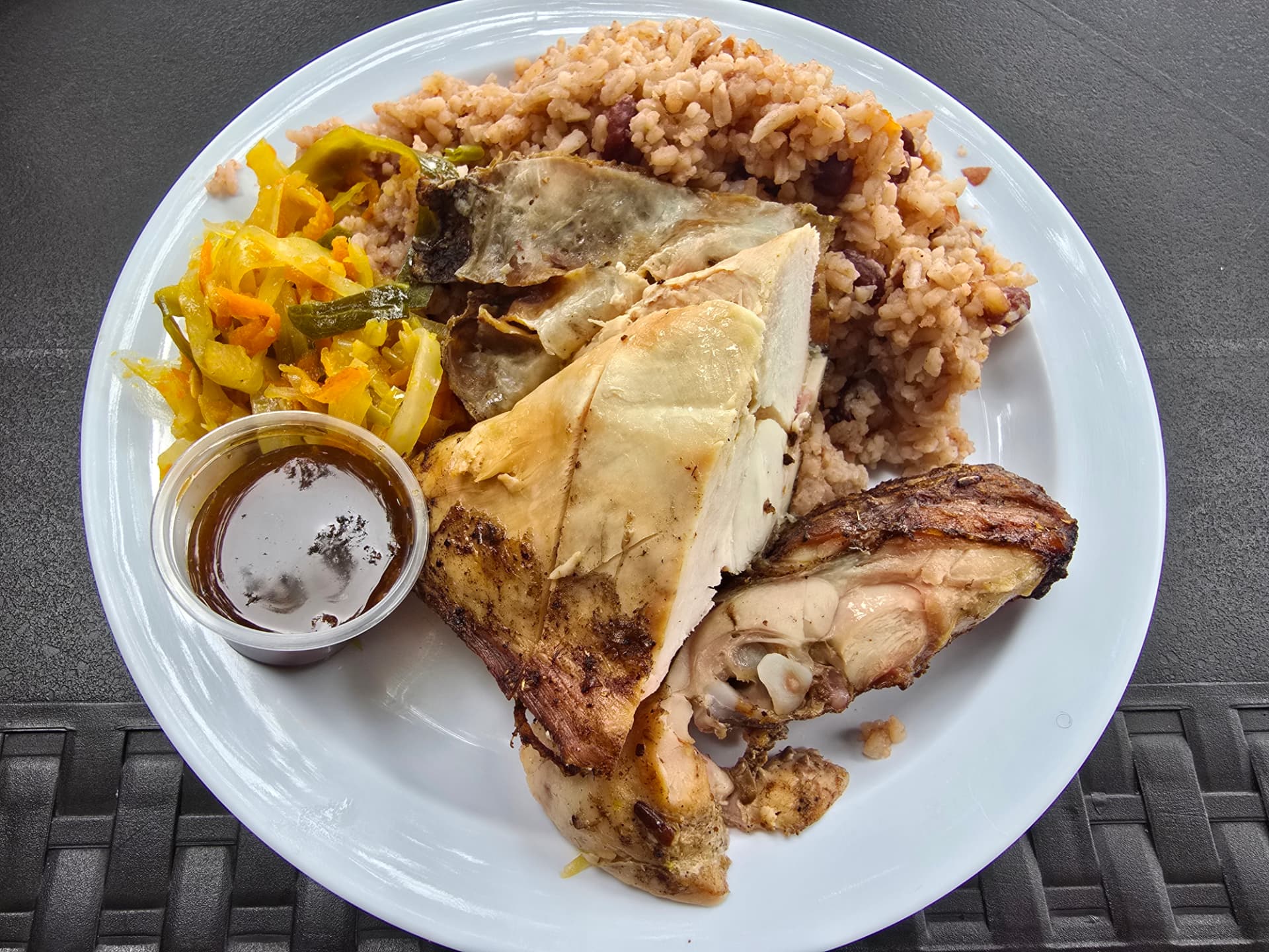 A plate of Jamaican jerk chicken with rice and peas and pickled vegetables.