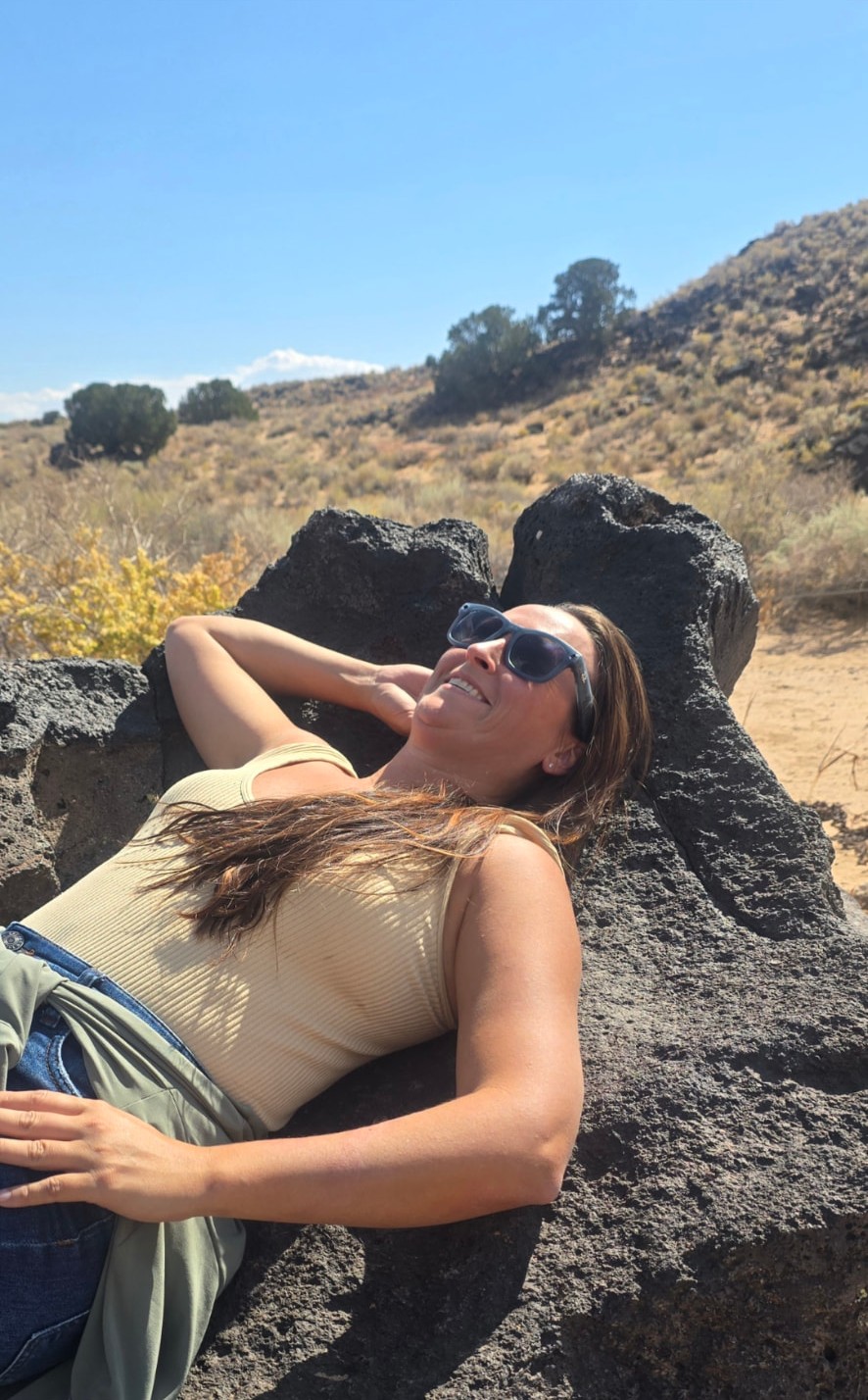 Nikki lying back on dark volcanic rock in the sun, smiling up at the sky.