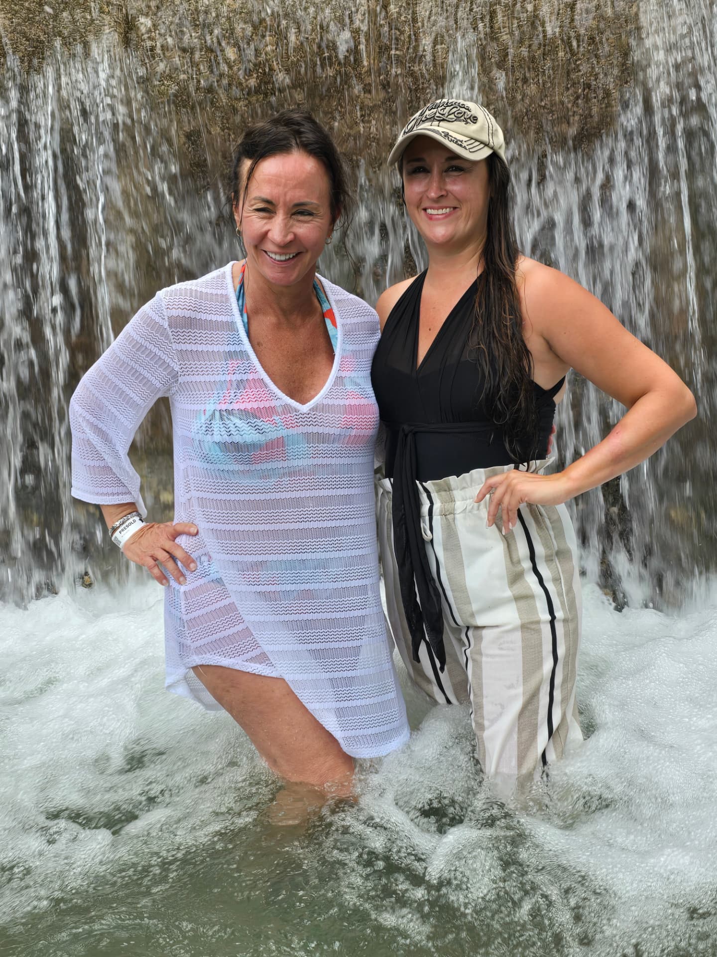 Patti and Nikki standing waist-deep beneath the falls, both smiling.