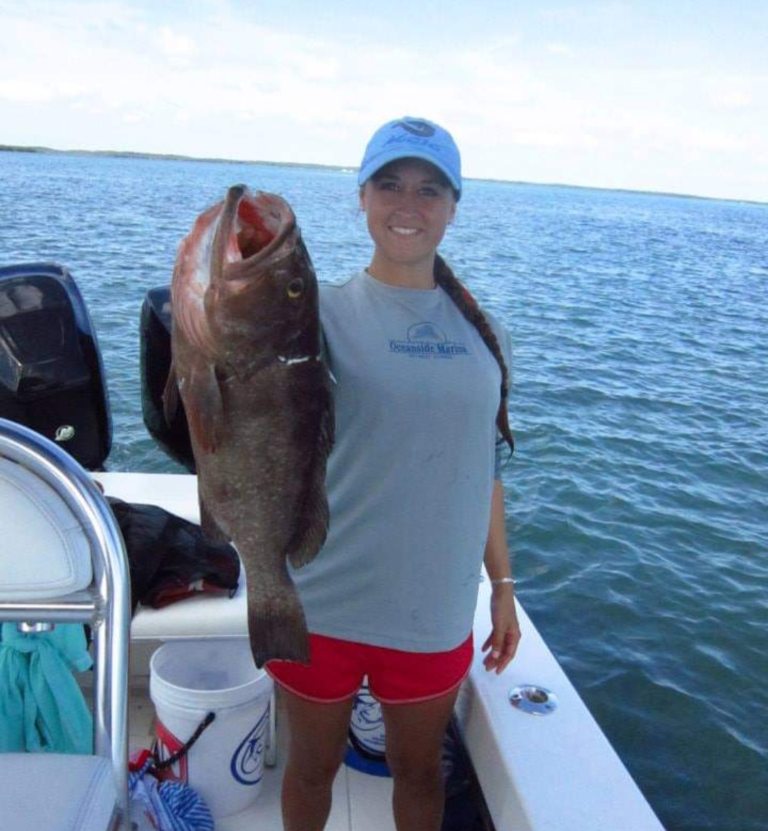 Nikki on a boat holding up a large grouper.