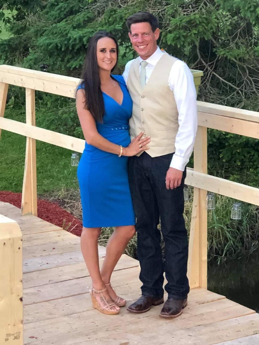 Nikki Bodie in a blue dress beside Quentin on a wooden footbridge in Wisconsin.