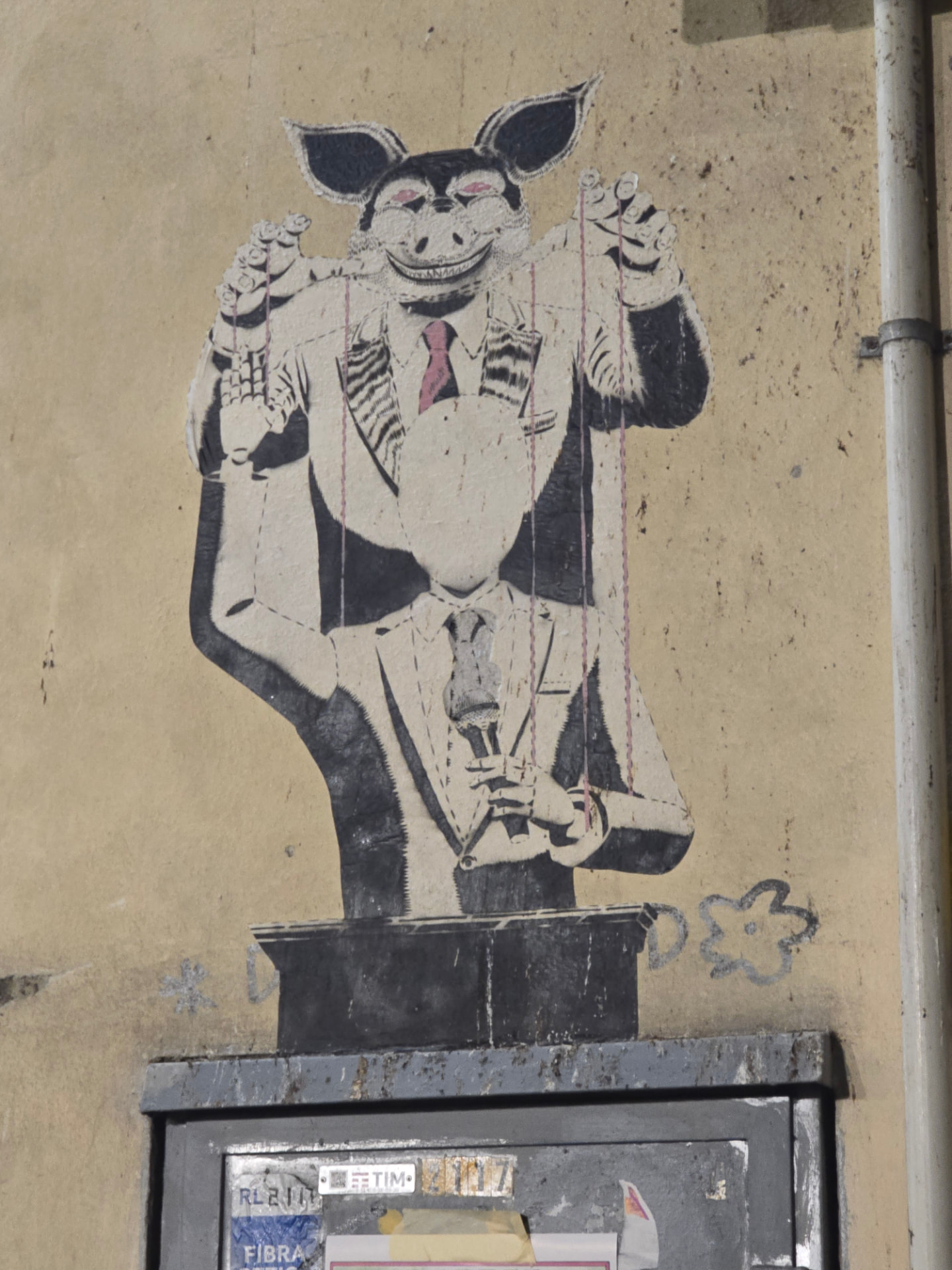 A paste-up of a grinning pig-eared figure working a faceless man in a suit like a puppet at a podium.