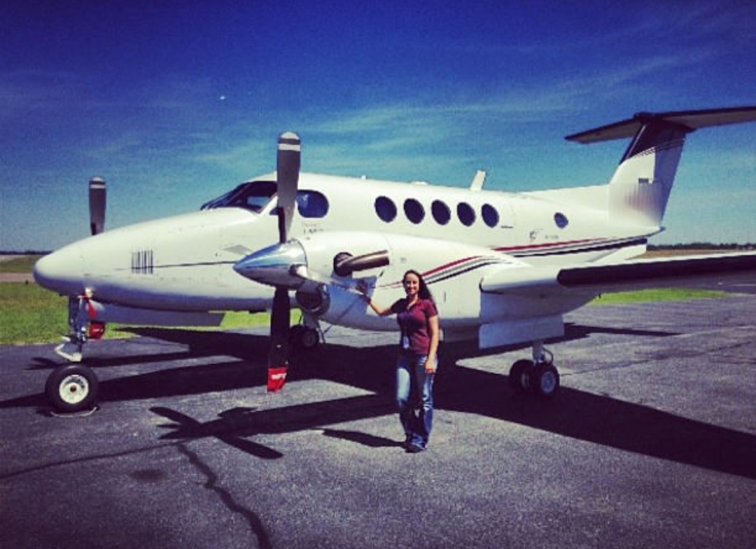 Nikki standing at the nose of a King Air under a deep blue sky.