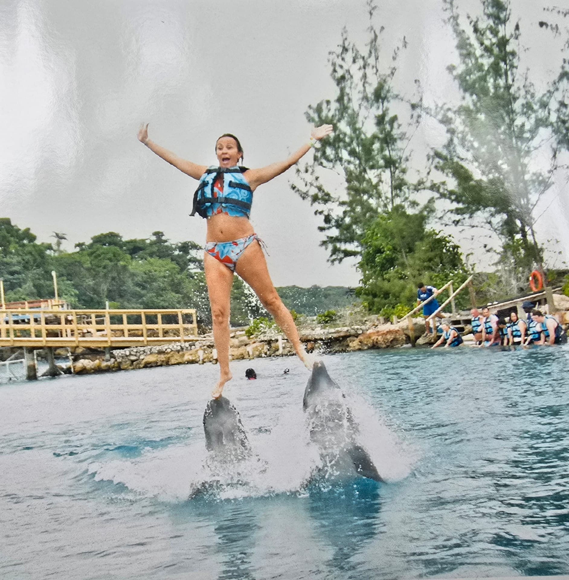 Patti launched into the air on the noses of two dolphins, arms out and mouth open.