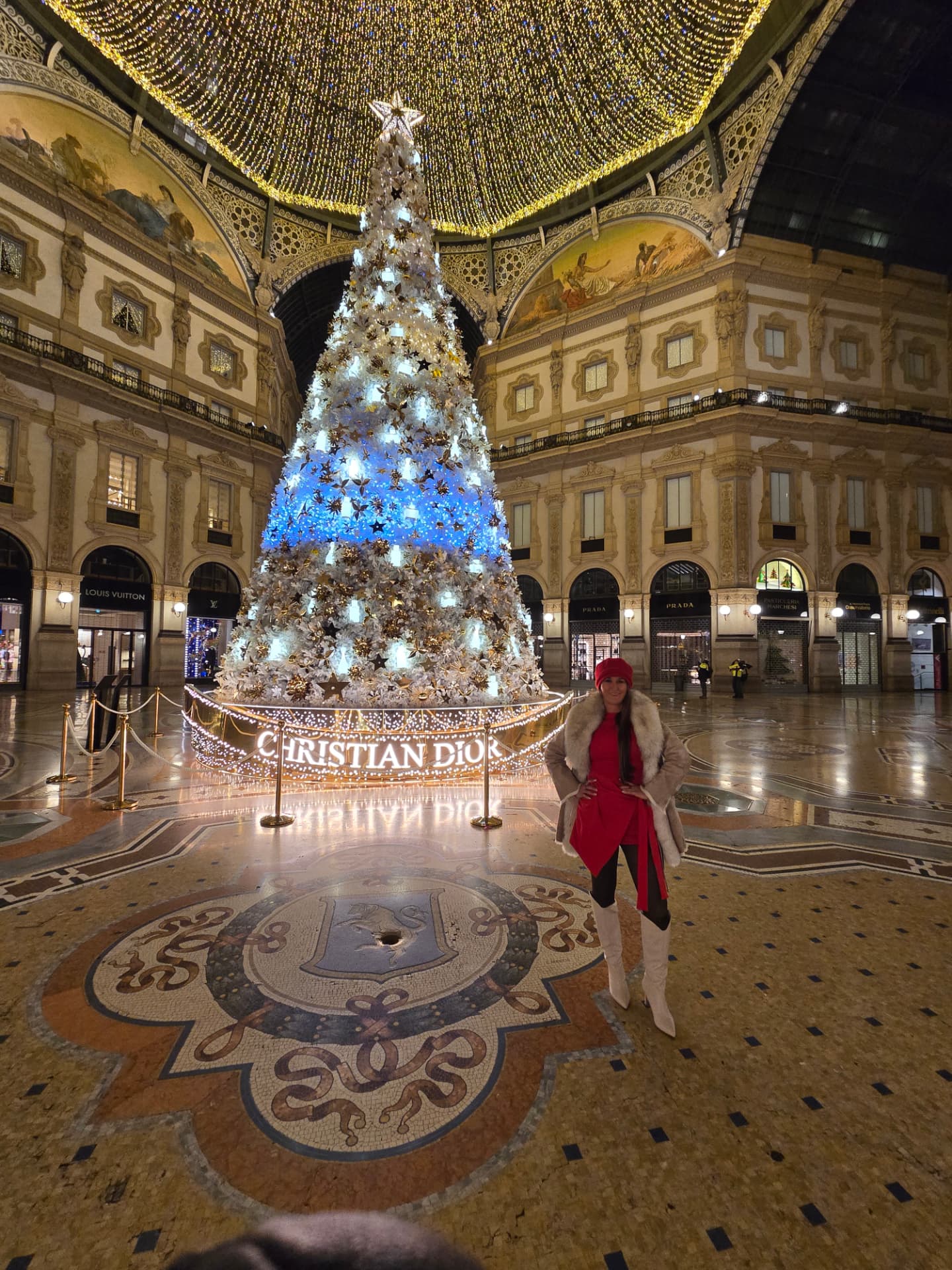 The Galleria Christmas tree glowing beneath the glass dome, Nikki Bodie in red standing beside it on the mosaic floor.