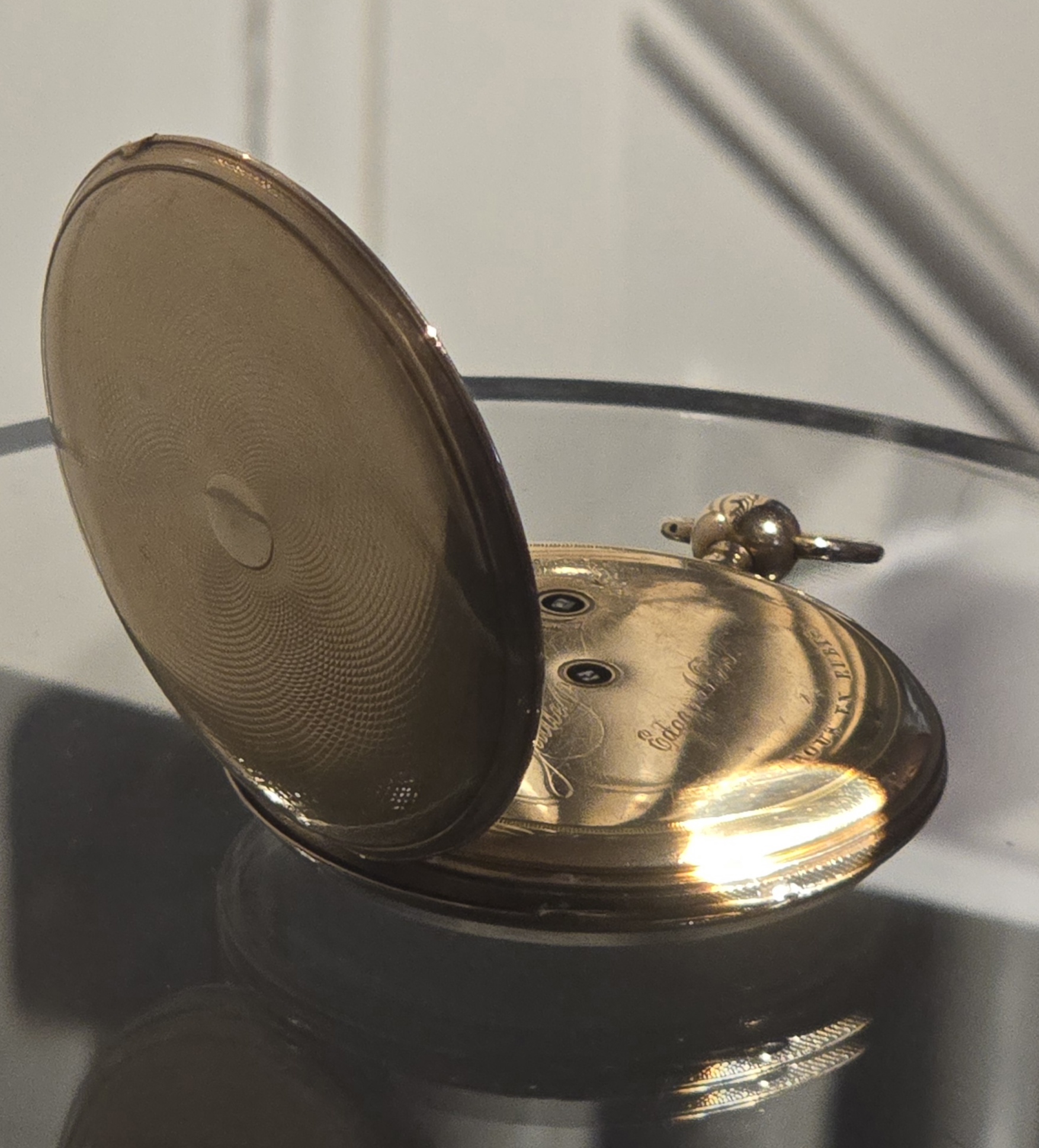 Edgar Allan Poe's gold pocket watch in a display case, its lid open to show the engraving inside.