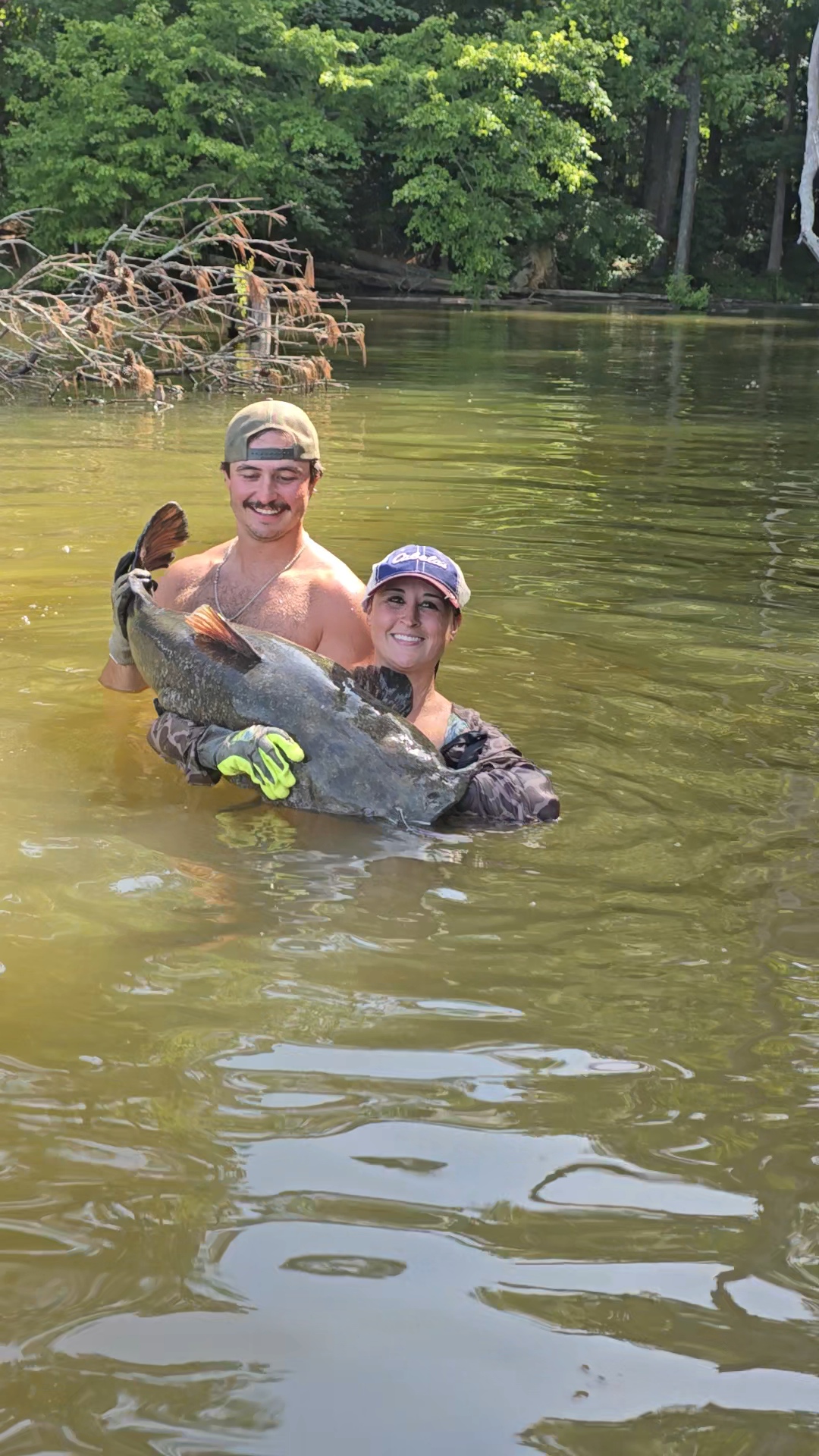 Nikki and Slayter chest-deep in the water holding an enormous catfish.