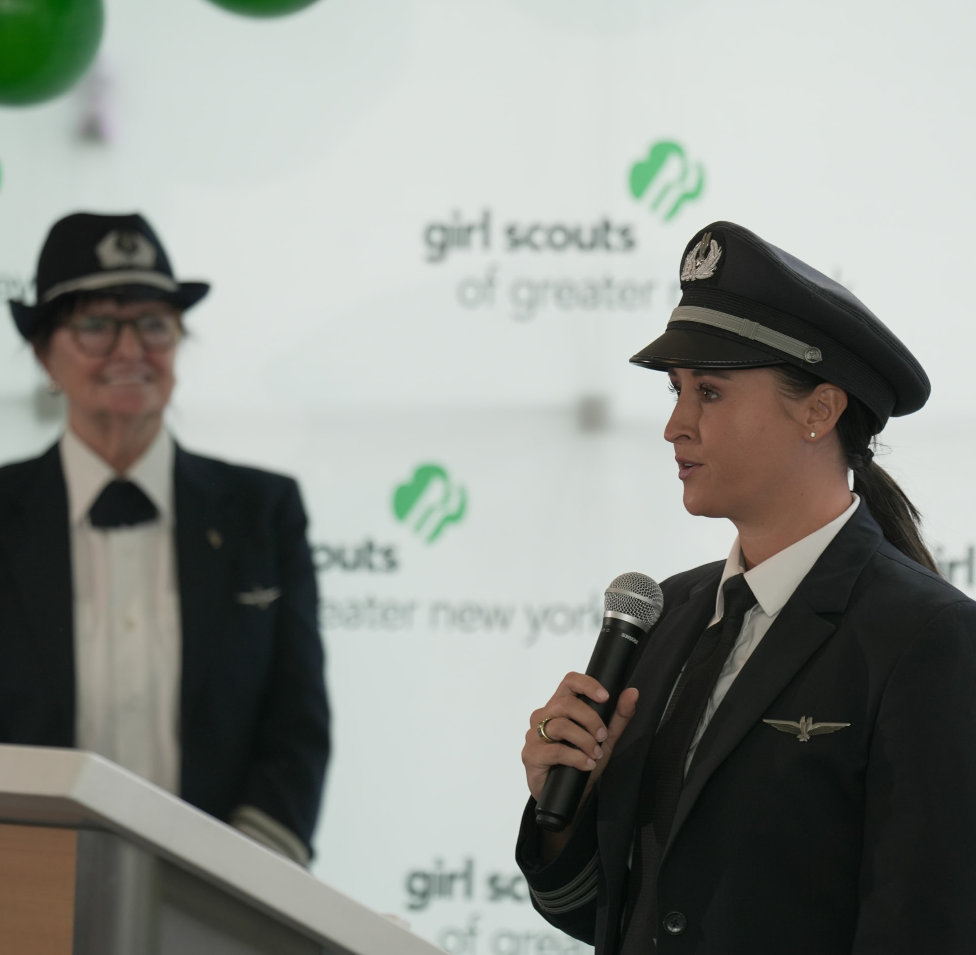 Nikki speaking at the Girl Scouts event as Bonnie Tiburzi listens behind her.