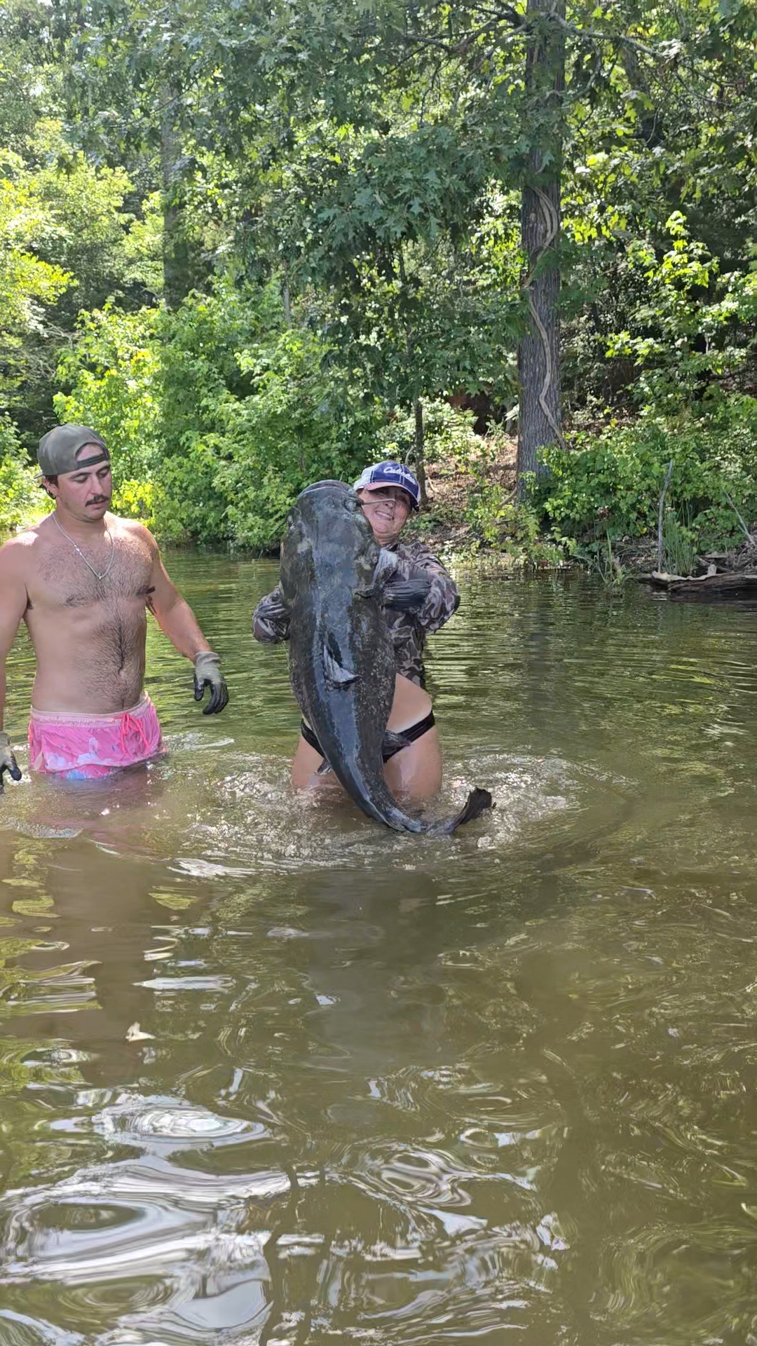 Nikki lifting an enormous catfish from the creek while Slayter looks on.