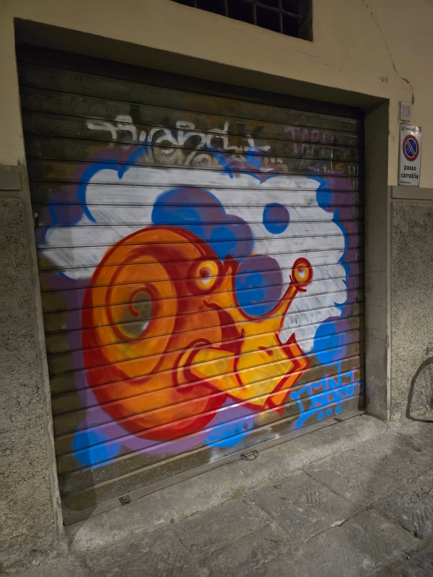 A bright orange spray-painted snail on a rolled-down metal shutter at night.