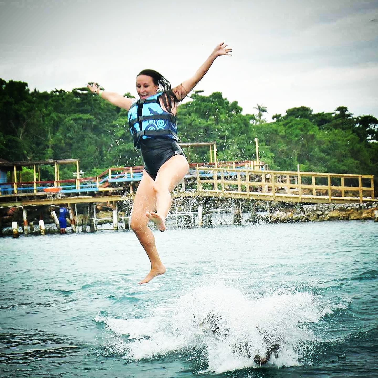 Nikki airborne over the water, one knee bent, laughing.
