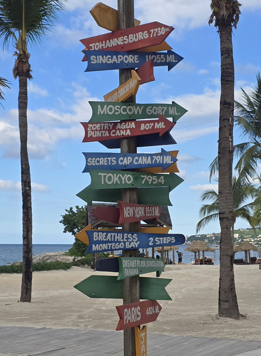 A colorful beach signpost of arrows pointing to cities around the world, one reading Breathless Montego Bay, 2 steps.