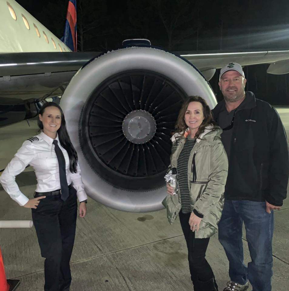 Nikki in uniform with her mom Patti and Ty Daddy beside a jet engine at night.