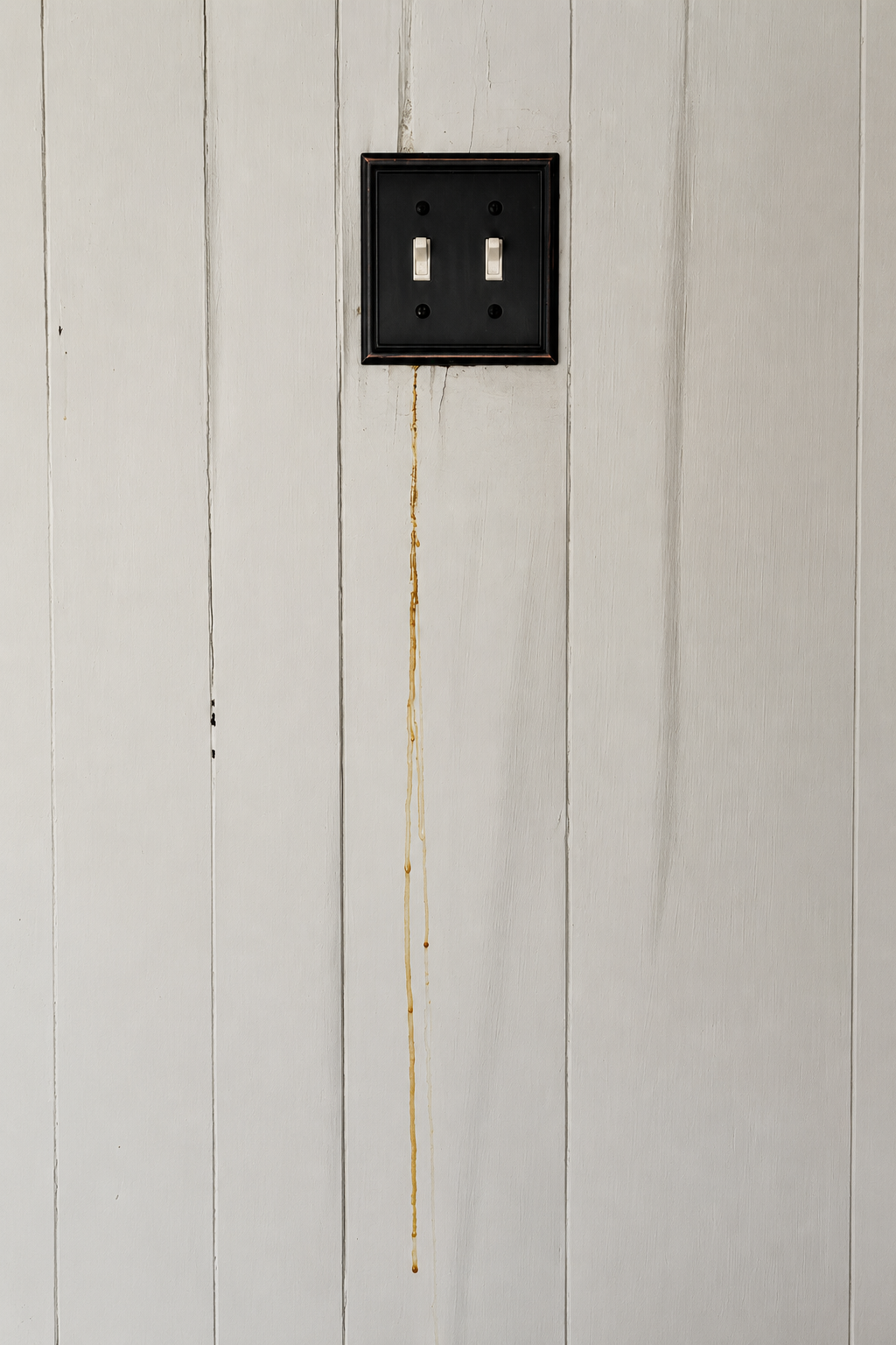 A white plank wall with a black double switch plate, two long amber trails running down from beneath it.