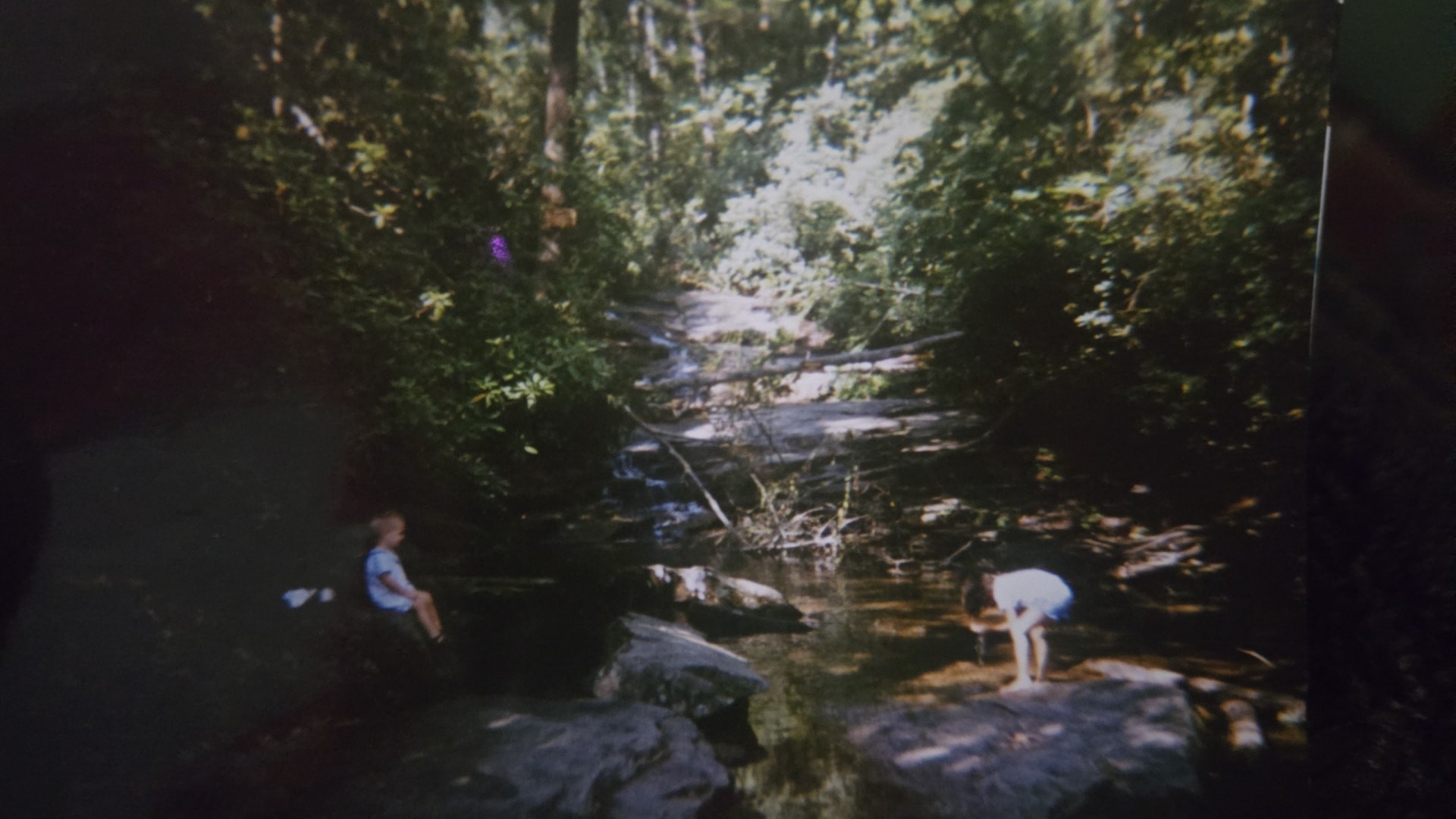 A faded photograph of Nikki and her brother Cheyenne playing on the rocks of a shaded creek.